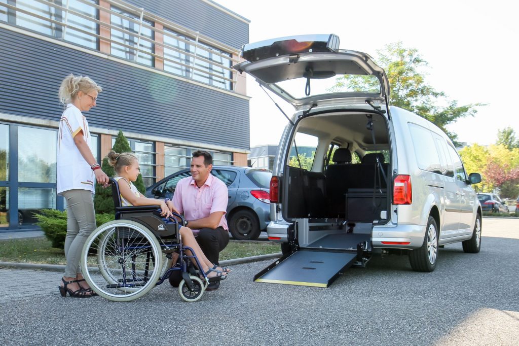 Deux adultes avec enfant en fauteuil roulant discutant devant voiture modulis 7 volkswagen caddy tpmr